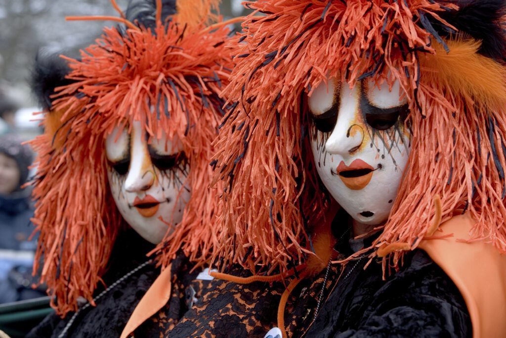 Two Fasnächtler (participants at the Carnival of Basel) in red-orange get-up, including traditional masks and costumes. Symbolic Image for Article: "Unmasking the Carnival of Basel: Traditional Costumes and Masks"
